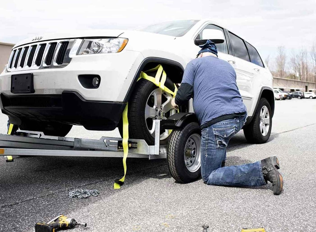 Technician securing white Jeep with professional towing straps on flatbed in Hollister, CA
